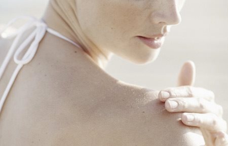 Donna che si applica la crema sulla spalla destra